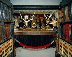 Edward & Nancy Kienholz / 
The Caddy Court (interior detail), 1986-1987 / 
mobile tableau: 1978 Cadillac with 1966 Dodge van, plaster casts, photographs, wood, metal, cloth, books, paint, polyester resin, light, shelves, curtain, antlers, animal skulls, taxidermy animal heads, clothing, furniture, clock, American flag, microphones, pitcher, glasses, gavel / 
84 x 276 1/2 x 100 in. (213.4 x 702.3 x 254 cm). 