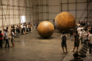 Sui Jianguo / 
Motion and Tension, 2009 / 
Steel structure and electrical machinery, iron balls / 
Height 98.43 in. (250 cm) / 
 / 
Viewers are confronted by oversized mobile steel spheres that /  are activated, yet confined within industrial steel walls, cages /  or the gallery space itself. These massive globes are set into /  motion against their enclosures, producing a jarring collision /  of metal, or a rolling, physical threat.  